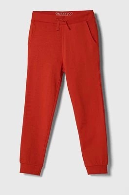 Zdjęcie produktu Guess spodnie dresowe bawełniane dziecięce kolor czerwony gładkie